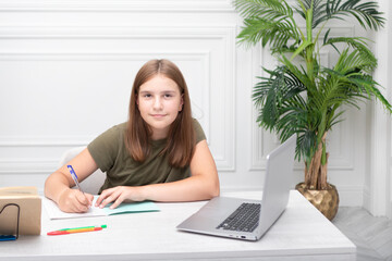 Portrait of lovely school girl sitting at the table and studying online. Distance education and preparation for school concept