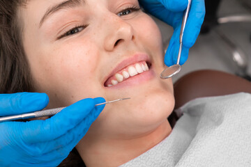 Cheerful lady showing her white teeth in a smile, a dentist brings dental instruments to her mouth with two hands