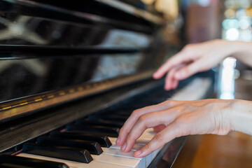 Hands of woman playing grand piano in musical school.Two hand with different level and keyboard.Blur background.Female pianist hands on grand piano keyboard.Playing music or song at home.