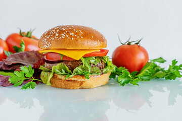 home cooked burger with cheese, tomatoes, chard and arugula on a white glass surface