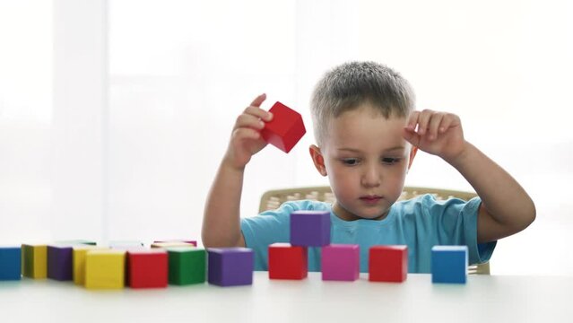 Adorable children play in kindergarten and at home. Colored cubes and toys on table. Child collects toys in kindergarten. Child home game. Concept of family happy.Kid with colored cubes plays at table