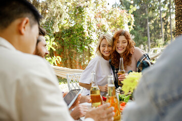 Two friends are having fun at a picnic table. A blonde and a redhaired girl are hugging on a picnic in the forest outside the city.