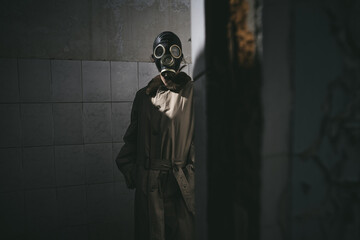 A man in gas mask standing inside an old building, peeking around the corner
