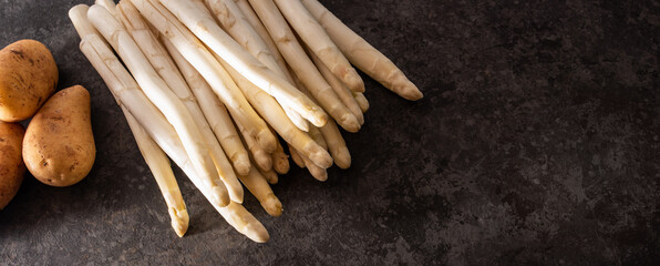 Fresh white asparagus and potatoes on black background. Spring vegetables on modern black kitchen plate. Seasonal gastronomy concept.