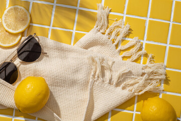 Lemon slices, sunglasses and a wool scarf arranged on yellow mosaic tiles background. Lemon (Citrus...