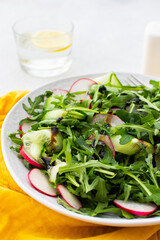 Healthy breakfasts, arugula and radish and cucumber salad with balsamic vinegar and olive oil, glass of water with lemon