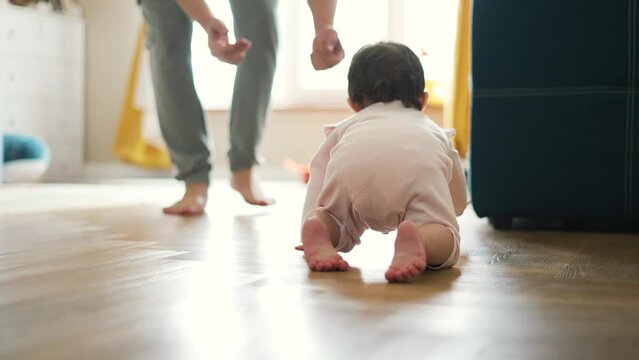 Happy and curious child explores his house by crawling on parquet floor.Father cheers his child up by clapping his hands.Baby crawls across floor towards his parent.Baby learn to move on floor at home