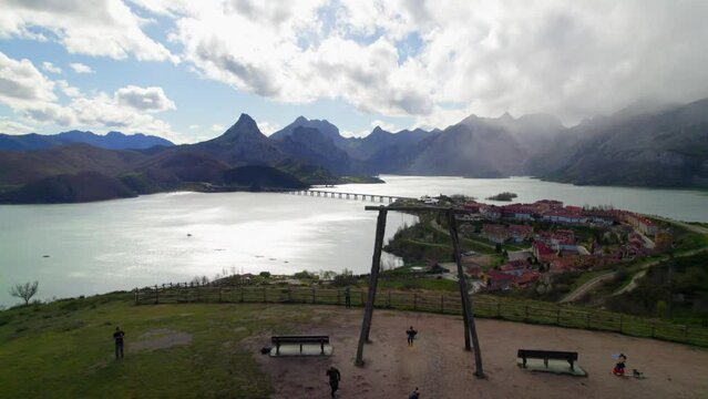 Fast aerial dolly shot with a family swinging their child on the swing at the viewpoint in Ria&ntilde;o, a village in Le&oacute;n, Spain on the shore of a large reservoir in the Cantabrian mountains.