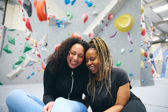 Two Smiling Female Friends Having Fun Laughing As They Try Climbing Wall At Indoor Activity Centre