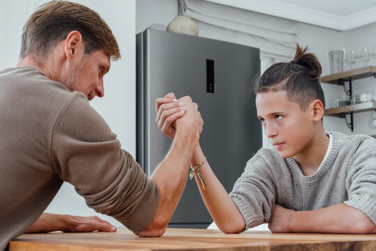 Father competing in arm wrestling with teen son, family spending time together. 