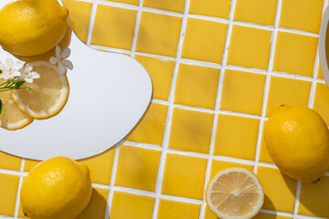Geometric mirror with Lemon slices and small white flowers displayed on. Blank space on yellow...