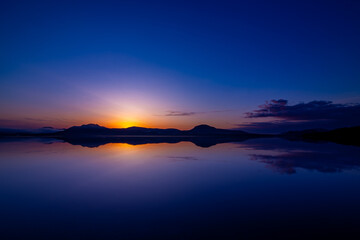 濃いブルーとオレンジ色の美しいグラデーションの夜明けの湖。