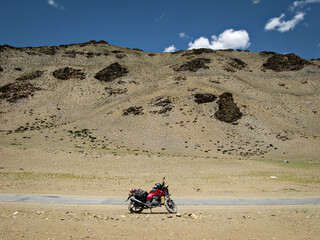 Obraz na płótnie Canvas Lone motorbike, motorcycle on adventurous road through besides river and mountains with clear blue sky on Manali to Leh highway in India