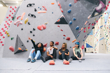 Group Of Friends Sitting On Floor Taking A Break After Exercise At Indoor Wall Climbing Centre