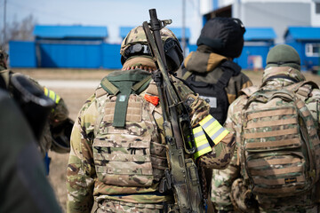 in the center from the back during the day, a soldier or a soldier of a special purpose unit in a helmet with a machine gun over his shoulder, other military men are walking nearby