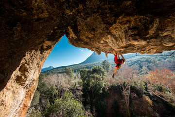 Girl climber on an overhanging rock. A sports woman climbs a rock against the backdrop of...