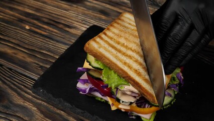 cutting a tall sandwich with ham, cheese and vegetables for breakfast or lunch. - Powered by Adobe