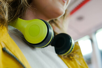 Close up of woman with yellow wireless headphones for music in public transport.