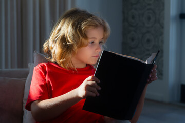 Portrait of cute blonde child reading interesting kids book story. Little child boy lying on the...