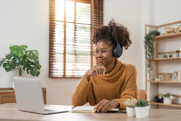 Image of cheerful african american woman using laptop and listen to music while sitting on chair in living room