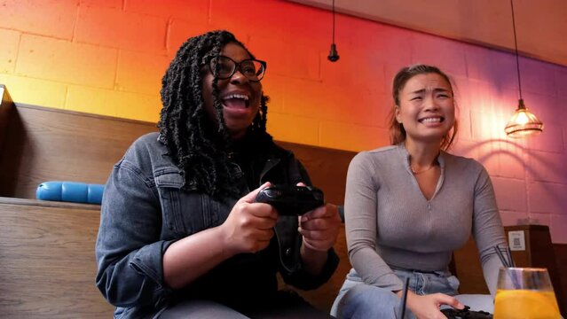 Female friends laughing while playing video game in bar