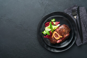 Steaks Osso Buco. Sliced beef grilled Osso Buco or porterhouse meat steak with garnished with salad and french fries on black marble board on old wooden background. Top view. Mock up.
