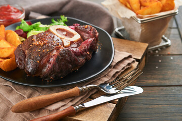 Steaks Osso Buco. Sliced beef grilled Osso Buco or porterhouse meat steak with garnished with salad and french fries on black marble board on old wooden background.