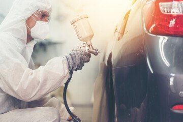 Automotive paint services, quality auto body shop concept. Male car mechanic working with spray gun...