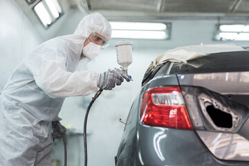 Automotive paint services, quality auto body shop concept. Male car mechanic working with spray gun...