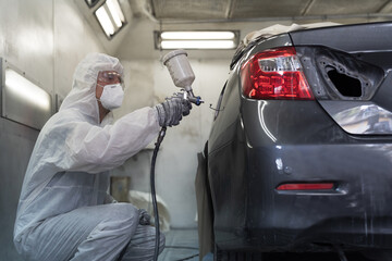 Automotive paint services, quality auto body shop concept. Male car mechanic working with spray gun...