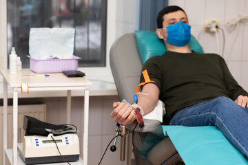 man donor in medical mask for bone marrow donation blood in laboratory. male hand holding red ball, prevention of diseases, illness hemodialysis transfusion in hospital. soft focus