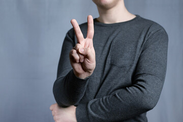 Young man shows victory sign of two fingers of his hand raised up. The gesture shows victory.