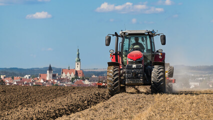Red tractor in field at plowing stubble and harrowing dirt in Czech landscape. Farm vehicle working...