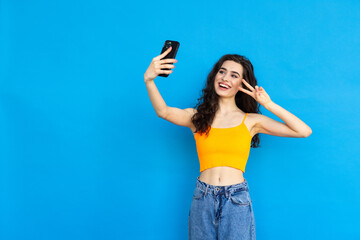 Emotional positive young pretty woman posing isolated over blue wall background take selfie by...