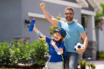 Sporty family. Excited father and son with winning gesture. Father helping son to ride a bicycle. Little kid boy in safety helmet learning to ride cycle with his dad. Fathers day.