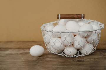 mesh metal basket with fresh white chicken eggs on wooden table, valuable food product, Easter...