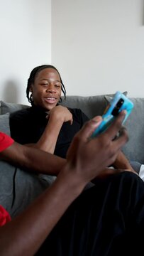 Teenage friends using smart phones and rough-housing on sofa at home