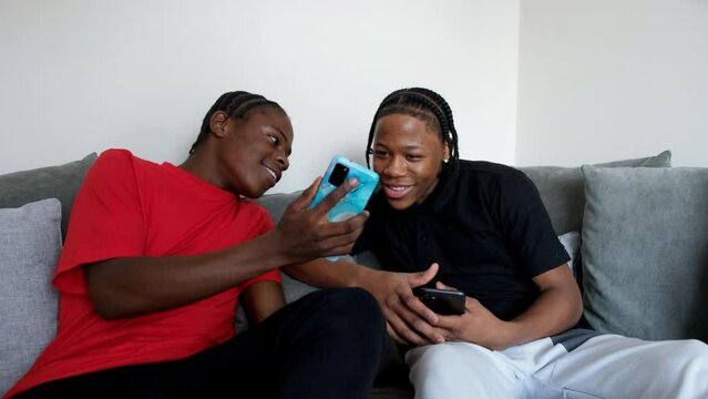 Teenage friends using smart phones and rough-housing on sofa at home