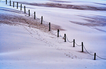 Shifting sand dune in national park near Leba with abstract graphic rope border on wooden poles