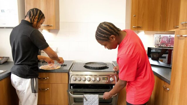 Teenage boys baking pizza in oven at home