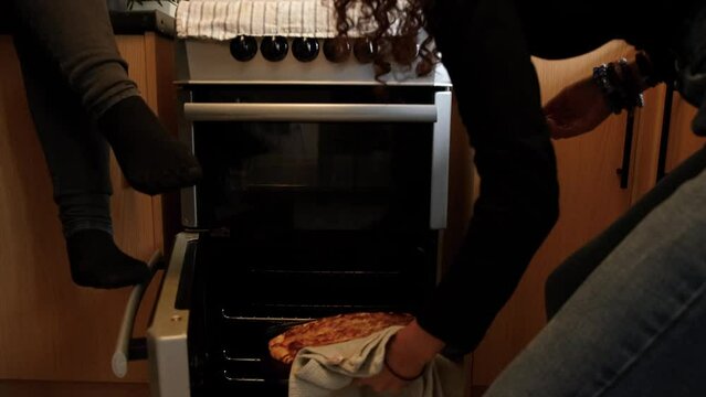 Teenage friends cutting baked pizza in kitchen at home