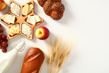 Jewish holiday Shavuot table top view. Flat lay cottage cheese, bread, bottle of milk, apple, cheese, wheat on white table.
