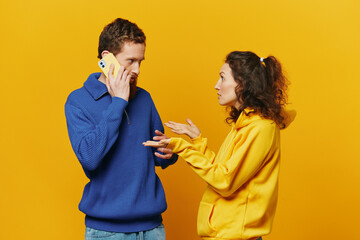 Man and woman couple with phone in hand call talking on the phone, on a yellow background, symbols signs and hand gestures, family quarrel jealousy and scandal.