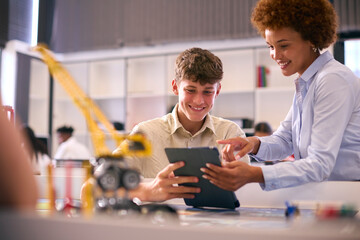 Female High School Teacher With Digital Tablet Helping Teenage Boy In STEM Technology Lesson