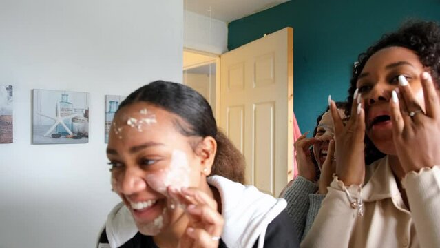Teenage friends applying cream and mask on face in bathroom