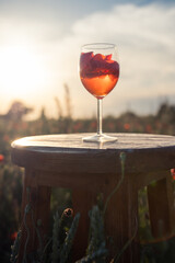 A glass of red drink stands on a wooden table in a field