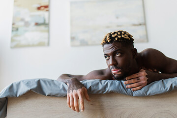 Young african american man with vitiligo lying on bed at home.