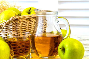 Green apples and jug with glass with apple juice on wooden background