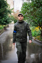 Portrait of serious military man in olive uniform and cap walking on street on rainy summer day
