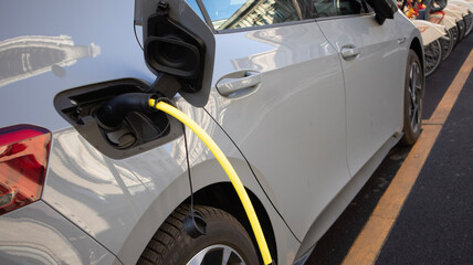 EV Car or Electric vehicle at charging station with the power cable supply plugged in on blurred nature with blue energy power effect. Eco-friendly sustainable energy